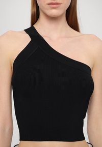 Crop top noir à côtes avec une bretelle. Présente un design ajusté et une texture lisse, mettant en valeur la silhouette élégante.