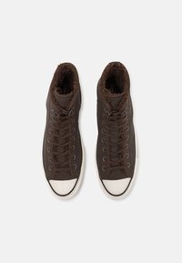 Hnědé vysoké tenisky s texturovaným svrškem, huňatou hnědou podšívkou a bílou gumovou špičkou. Obsahují tkaničky a kontrastní prošívání.