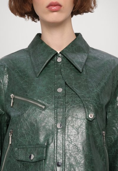 Giacca di pelle verde con una finitura texturizzata, dotata di un ampio colletto, bottoni a pressione e una tasca sul petto con zip.