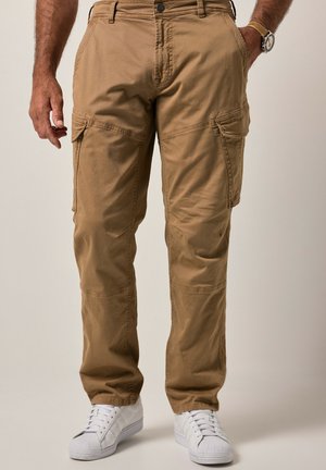 Beige Cargo-Hosen mit Seitentaschen, aus durablem Baumwollmaterial. Gerades Bein-Design mit subtilen Nähten. Getragen mit weißen Sneakern.