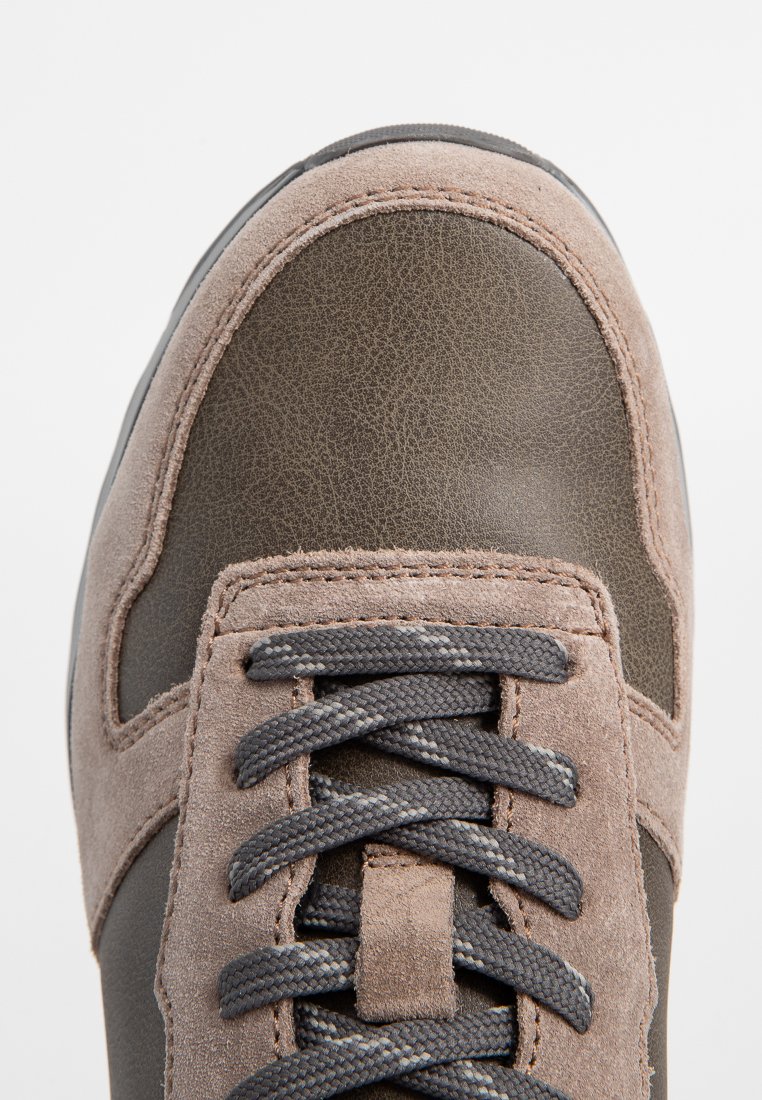 Sneaker en cuir marron et daim avec un bout arrondi, des lacets gris et des coutures beiges. Présente un dessus lisse et des accents texturés.