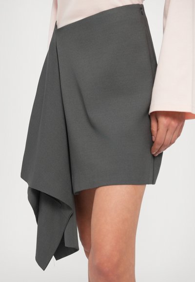 Szürke aszimmetrikus szoknya, redőzött elülső szegéllyel, texturált szövettel és rejtett oldalsó záródással. Sima kivitel, térd alá érő fazon.