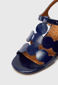 Σανδάλι από γαλακτερό δέρμα σε ναυτικό μπλε με λουριά με κυματιστά άκρα και αγκράφα στον αστράγαλο, εσωτερική σόλα ταμπά με επένδυση, κοντινή λήψη στην περιοχή των δακτύλων.