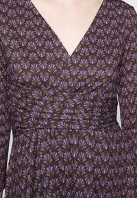 Sukienka w kształcie litery A z ciemnej tkaniny, z powtarzającym się wzorem fioletowych i złotych liści. Dekolt w kształcie V, długie rękawy oraz marszczony pasek w talii.