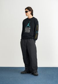 Must have sinine ja valge graafikaga must dress; laiad mustad püksid; mustad kingad; mudel kannab prille. Sinine vaip taustana.