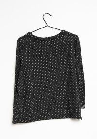 Maglietta nera a maniche lunghe con pois bianchi, caratterizzata da un colletto tondo e spacchi laterali, appesa a un gancio nero su uno sfondo bianco.