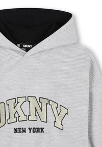 Haut à capuche en gris texturé avec un intérieur noir, présentant un lettrage « DKNY » en relief en or et noir. Étiquette visible à l'intérieur du col.