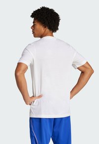 Vit t-shirt med kort ärm, rund halsringning, slät textur, något lös passform, med blå shorts och synliga sidsömsdetaljer.