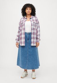 Cămașă din flanel în carouri, albă, roz și albastră; asortată cu o fustă lungă din denim și adidași. Cămașa dispune de două buzunare la piept.