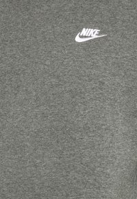 Graues Baumwoll-T-Shirt mit einem kleinen weißen Nike-Logo auf der linken Brustseite; glatte Textur und klassisches Rundhalsausschnitt-Design.