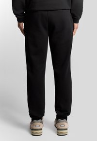 Sorte sweatpants med en afslappet pasform. Fremstillet af blødt stof, med snøre i taljen og ribbede manchetter. Båret med beige sportssko.