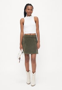 Un haut court blanc avec un ourlet festonné, associé à une mini-jupe en velours côtelé vert olive. Un sac à main blanc et des bottes de cowboy blanches avec des accents floraux.