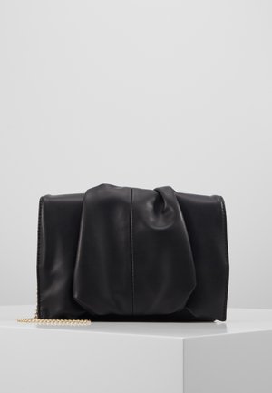 Zwarte zachte leren clutch met gerimpeld detail en gouden kettingriem, weergegeven op een witte ondergrond tegen een lichtgrijze achtergrond.