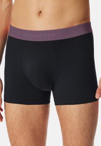 Boxer briefs neri in cotone con una cintura elastica di un viola scuro che presenta la parola "SCHIESSER" intessuta nella banda. Texture liscia, design aderente.