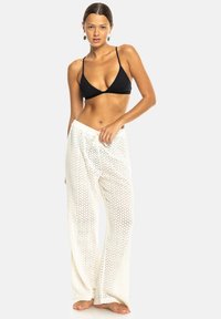 Zwarte bikini-top gecombineerd met losse, witte haakbroek. De broek heeft een textuurpatroon en een elastische tailleband.