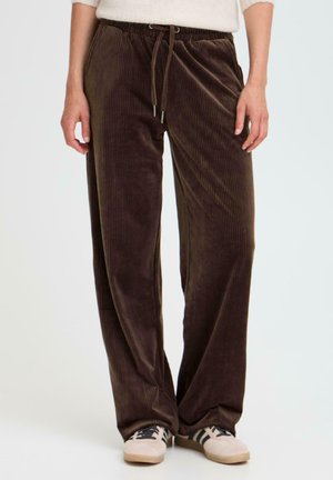 Pantalons en velours côtelé marron avec une coupe décontractée, dotés d'une taille à cordon de serrage, de rayures verticales et d'une texture lisse, portés avec des chaussures de couleur claire.