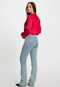 Blusa di raso rosso con maniche lunghe e cucitura posteriore, abbinata a jeans svasati blu chiaro con tasche posteriori e vita aderente.