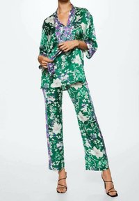 Set coordinato floreale verde composto da una maglietta dal taglio ampio con dettagli viola e pantaloni a gamba larga, realizzati in un tessuto liscio e lucido.