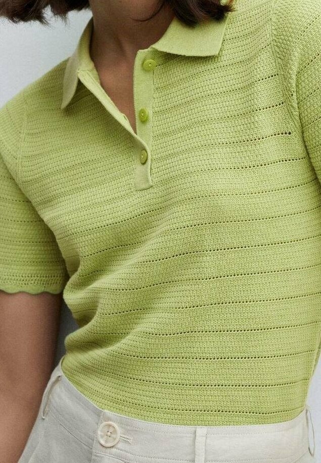 Femme portant un polo en maille vert clair à manches courtes avec trois boutons et des bords festonnés, associé à un pantalon blanc taille haute.