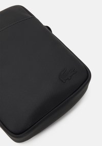 Borsa nera con trama e finitura liscia, bordi arrotondati e logo in rilievo discreto. Progettata per una conservazione compatta e facile accesso.