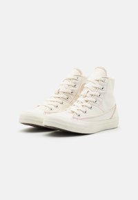 Wysokie trampki wykonane z off-white płótna. Cechy to metalowe oczka, białe gumowe podeszwy oraz kontrastowe brzoskwiniowe szwy.