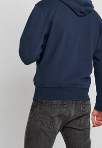 Sudadera navy hecha de una mezcla de algodón suave, con dobladillos y puños acanalados, combinada con jeans gris oscuro que cuentan con bolsillos traseros clásicos y detalles de costura.