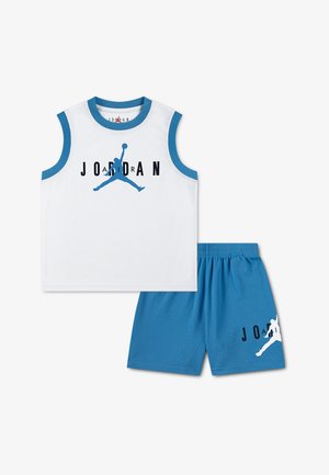 Camiseta de baloncesto blanca sin mangas con ribetes azules y logo de Jordan, combinada con pantalones cortos azules que llevan un logo más pequeño de Jordan.