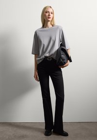 T-shirt grigia oversize, vestibilità rilassata, maniche corte; jeans neri svasati classici, texture liscia; borsa nera grande con finitura testurizzata.