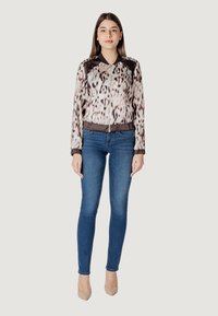 Giacca bomber leggera con un motivo in pelle di leopardo in crema e marrone, dotata di zip frontale e polsini a costine, abbinata a jeans skinny blu.