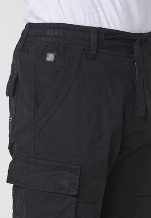 Black cargo shorts feature a drawstring waistband, side pockets, and a textured fabric with a small logo patch on the front.