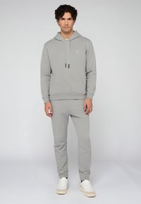 Světle šedá mikina a souprava tepláků s přední kapsou, šňůrkami a manžetami. Vyrobeno z měkké, texturované tkaniny.