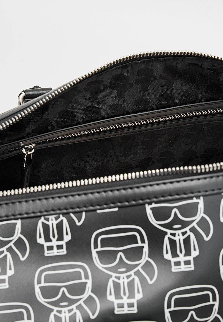 Bolso negro con figuras de dibujos animados blancas. Exterior liso, cierre con cremallera y un forro interior negro texturizado con un patrón sutil.