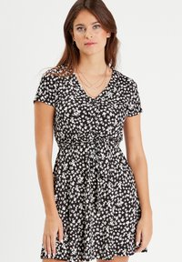 Schwarzes kurzärmeliges Kleid mit V-Ausschnitt und weißem Blumenmuster. Verfügt über eine taillierte Taille mit einem geknoteten Detail und einem fließenden Rock.