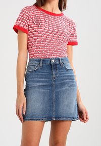 Camiseta de patrón rojo y blanco con cuello redondo, combinada con una falda mini de mezclilla que presenta bolsillos frontales y un acabado en azul desgastado.