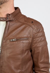 Braune Lederjacke mit schlankem Design, hohem Kragen und Reißverschluss vorne. Verfügt über Schulterakzente und strukturierte Stickerei an den Ärmeln.