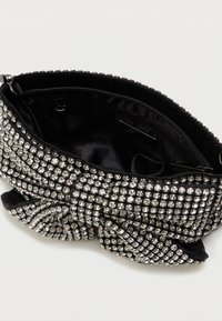 Czarna torebka kopertówka pokryta rzędami błyszczących cyrkonii, z dużą kokardą i widoczną kieszenią na zamek błyskawiczny w środku.
