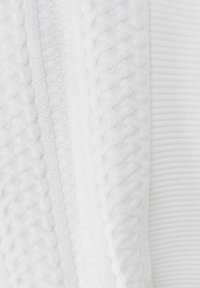 Weißes Textil mit gerippten und gewebten Mustern, sichtbaren Nähten und texturierten Akzenten entlang der Kanten.