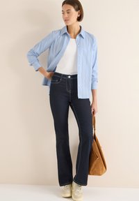 Lyseblå stribet skjorte med knapper over en hvid tanktop, kombineret med mørke, vidde jeans og beige sneakers. En brun ruskindstaske er inkluderet.