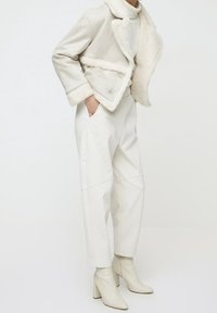 Chaqueta de forro de borrego crema combinada con pantalones blancos de tiro alto y botas de tobillo beiges. El conjunto presenta líneas limpias y un ajuste estructurado.