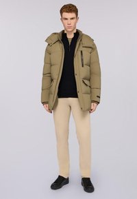 Chaqueta puffer color caqui con capucha, bolsillos con cremallera y botones a presión en la parte delantera, combinada con pantalones beis claros y zapatillas negras.