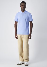 Jasnoniebieska koszulka polo z trzema guzikami, zestawiona z beżowymi spodniami o szerokich nogawkach i białymi sneakersami z szarymi akcentami. Gładka tekstura, casualowy design.