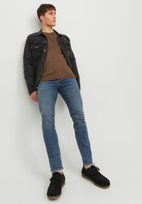 Veste en denim noir sur un pull en laine texturé brun, assortie à un jean bleu slim et des chaussures en suédine noires avec une semelle brun clair.