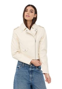 Giacca cropped in finta pelle bianca con chiusura a zip, spalline, tasche laterali e dettagli a pressione; abbinata a jeans blu a vita alta.