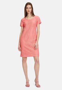 Knee-langes, kurzärmliges Kleid in Koralle mit einem strukturierten Karomuster. Der Stoff wirkt leicht. Kombiniert mit rosa Riemchenheels.