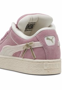 Sneaker din suede roz cu o talpă din cauciuc texturat alb, având un detaliu mic sub formă de fundiță pe lateral și un patch cu logo pe toc.
