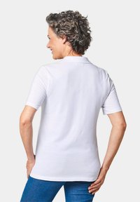 Witte polo met korte mouwen en een kraag, met een gladde textuur en een getailleerde pasvorm, gedragen met blauwe denim broek, gezien van achteren.