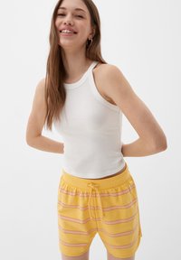 Weißes, geripptes Tanktop, kombiniert mit gelben Shorts mit horizontalen pinken Streifen. Die Shorts haben einen elastischen Taillenbund und einen Kordelzug.