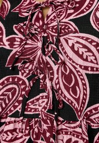 Stoff mit großen rosa und burgunderfarbenen Blumen- und Blättermustern auf schwarzem Hintergrund, mit gebundenen Stoffbändern in der Mitte.