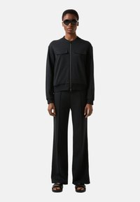 Schwarze Bomberjacke mit Reißverschluss, zwei Brusttaschen, passenden weit geschnittenen Hosen und flachen Sandalen. Glattes Gewebe mit lockerem Schnitt.