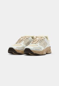 Pair of beige and white athletic shoes with thick brown soles placed side by side on a plain white background.